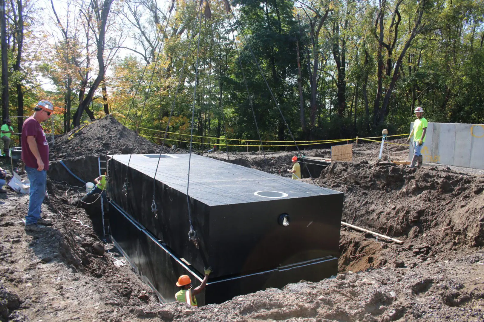 Workers install large black tank in dirt.